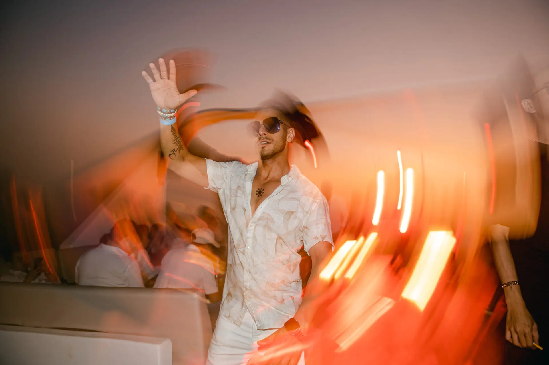 Man in white dancing among trailing light streaks at a sunset deck party
