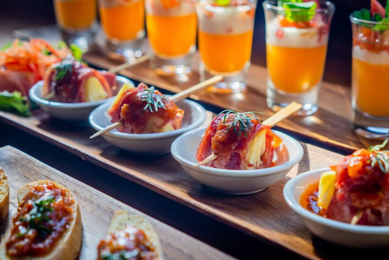 Plated canapés and orange cocktail shots on a wooden serving board