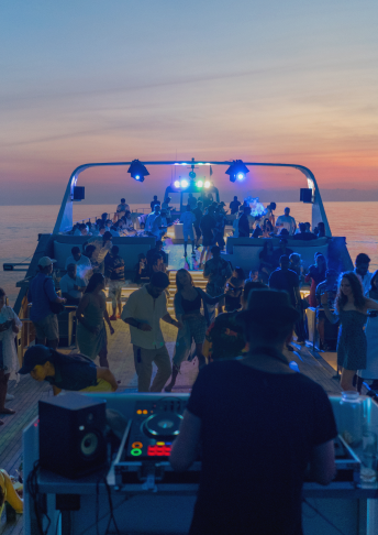 Guests at a sunset deck party aboard The Shivanna with DJ booth and blue stage lights