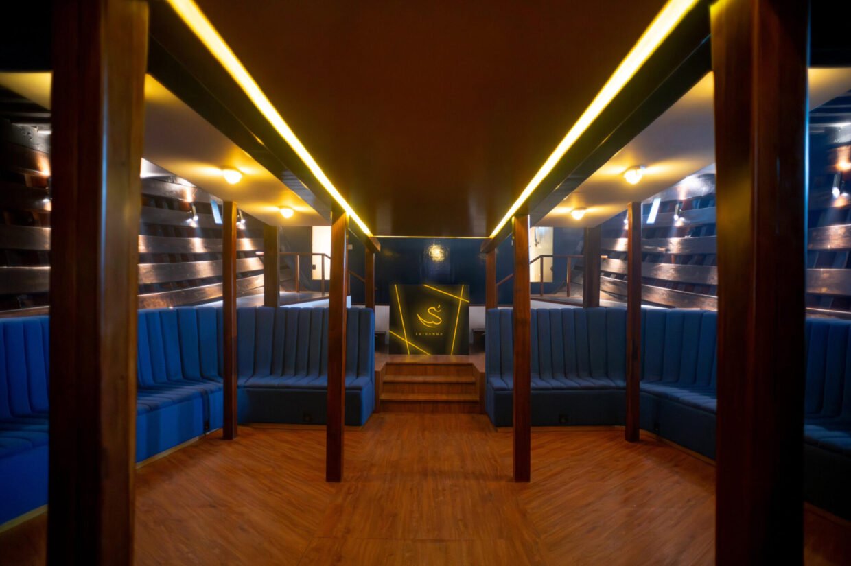 Lower deck lounge with blue banquette seating and gold Shivanna emblem under accent lighting