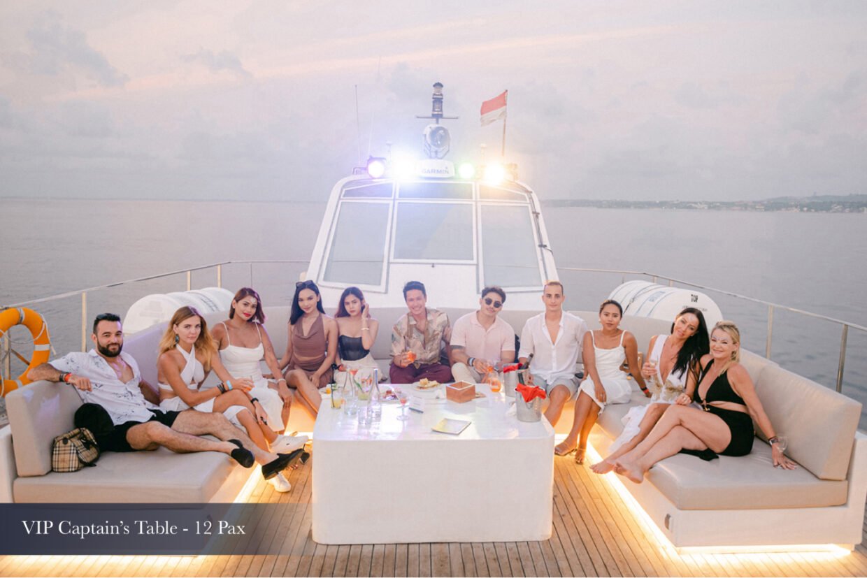 Twelve guests lounging at the VIP Captain's Table on the yacht deck at dusk