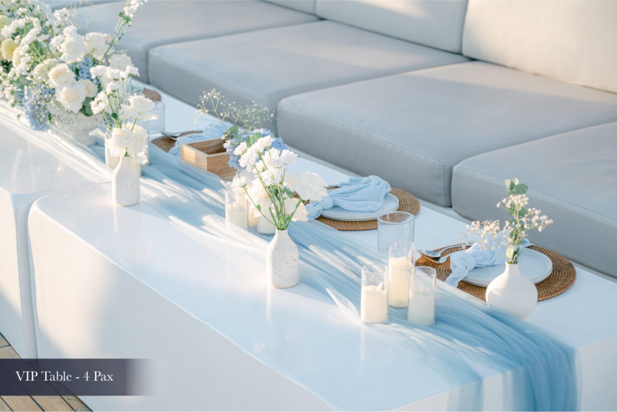 Blue-themed VIP table setting with white florals and candles on deck