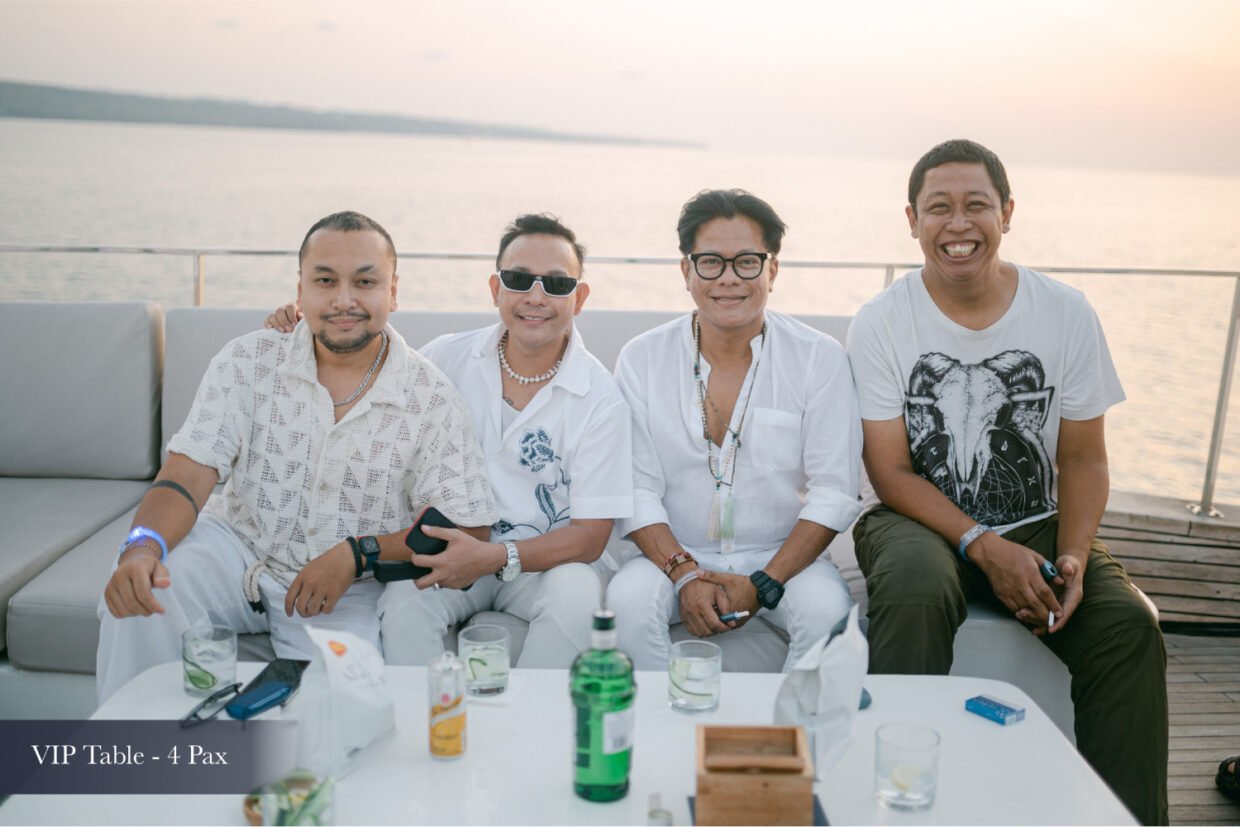 Four men in white relaxing with drinks at a VIP table at sunset