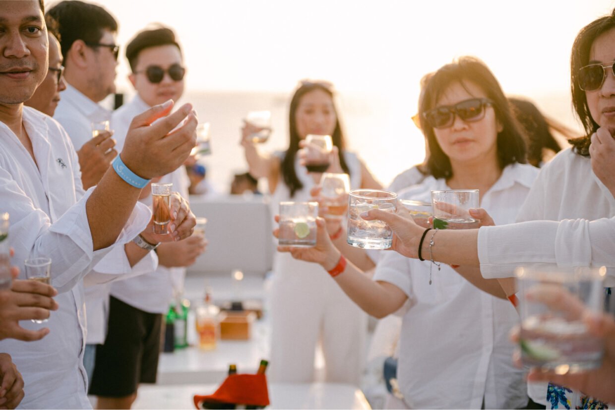 Guests in white clinking cocktail glasses in golden sunset light