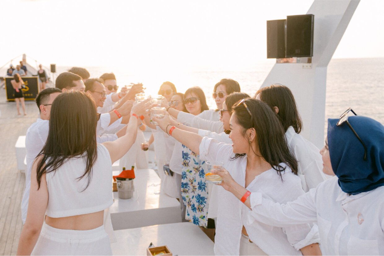 Guests in white raising a group toast on the deck at sunset