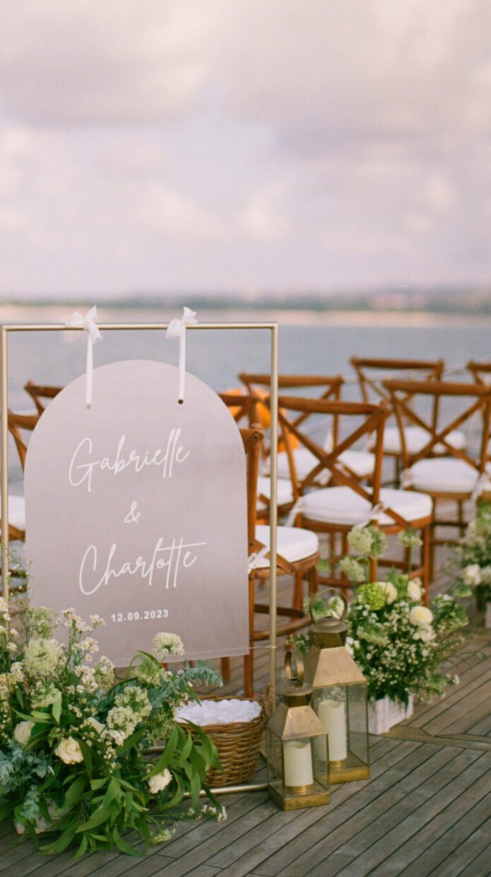 Arched welcome sign "Gabrielle & Charlotte 12.09.2023" at a deck wedding ceremony