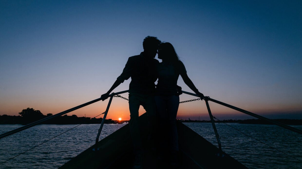 Couple silhouetted at the boat bow against an orange sunset