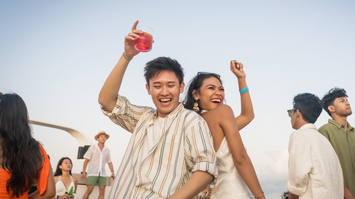Two guests laughing and dancing with drinks aboard at dusk