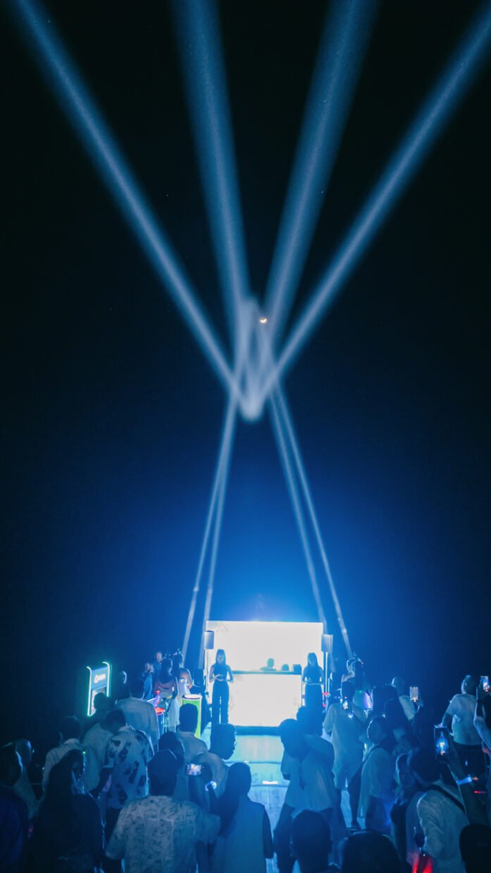 Crowd watching a stage lit by crossing laser beams at a nighttime deck party