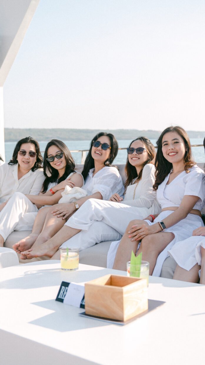 Group of women in white seated on a VIP sofa in bright sunlight
