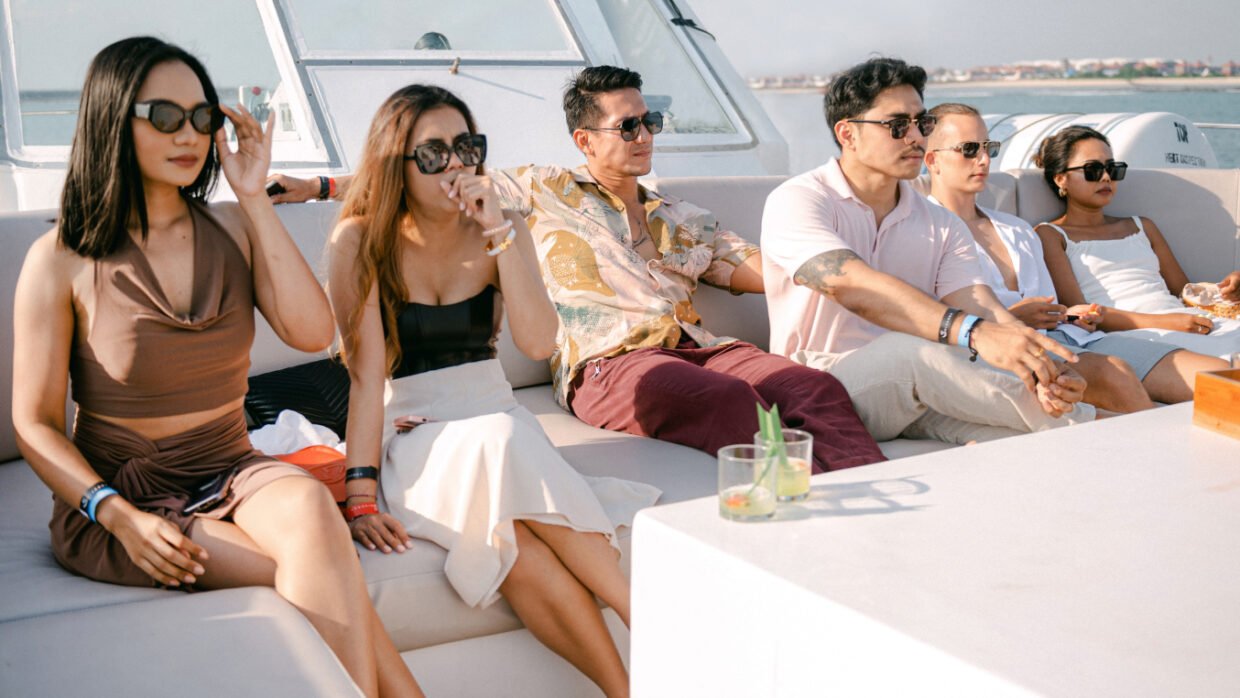 Row of stylish guests in sunglasses seated on deck, Nusa Dua behind