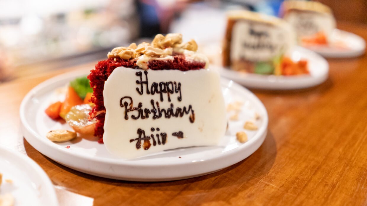 Red velvet slice iced "Happy Birthday Aji" plated on a wooden table