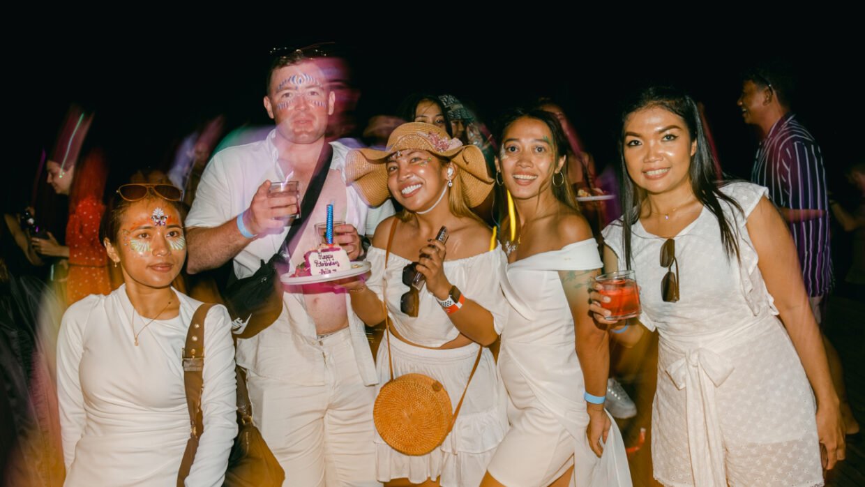 Guests in white posing with a birthday cake at a nighttime deck party