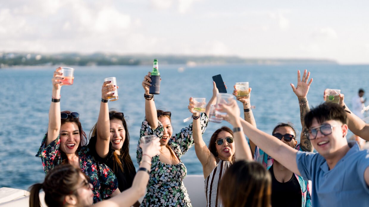 Women cheering and raising drinks on deck with the bay behind