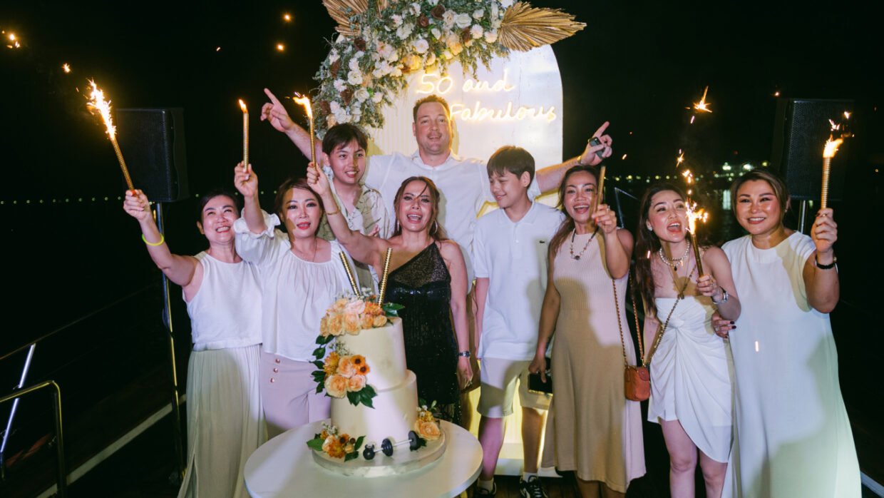 Guests with sparklers around a tiered "50 and Fabulous" birthday cake on deck at night