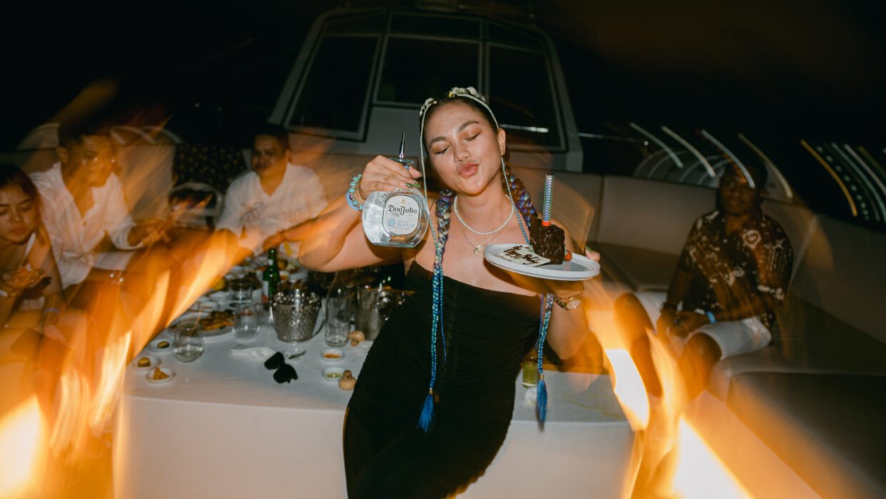 Woman holding a Don Julio bottle and chocolate cake slice at a fire-lit dinner party