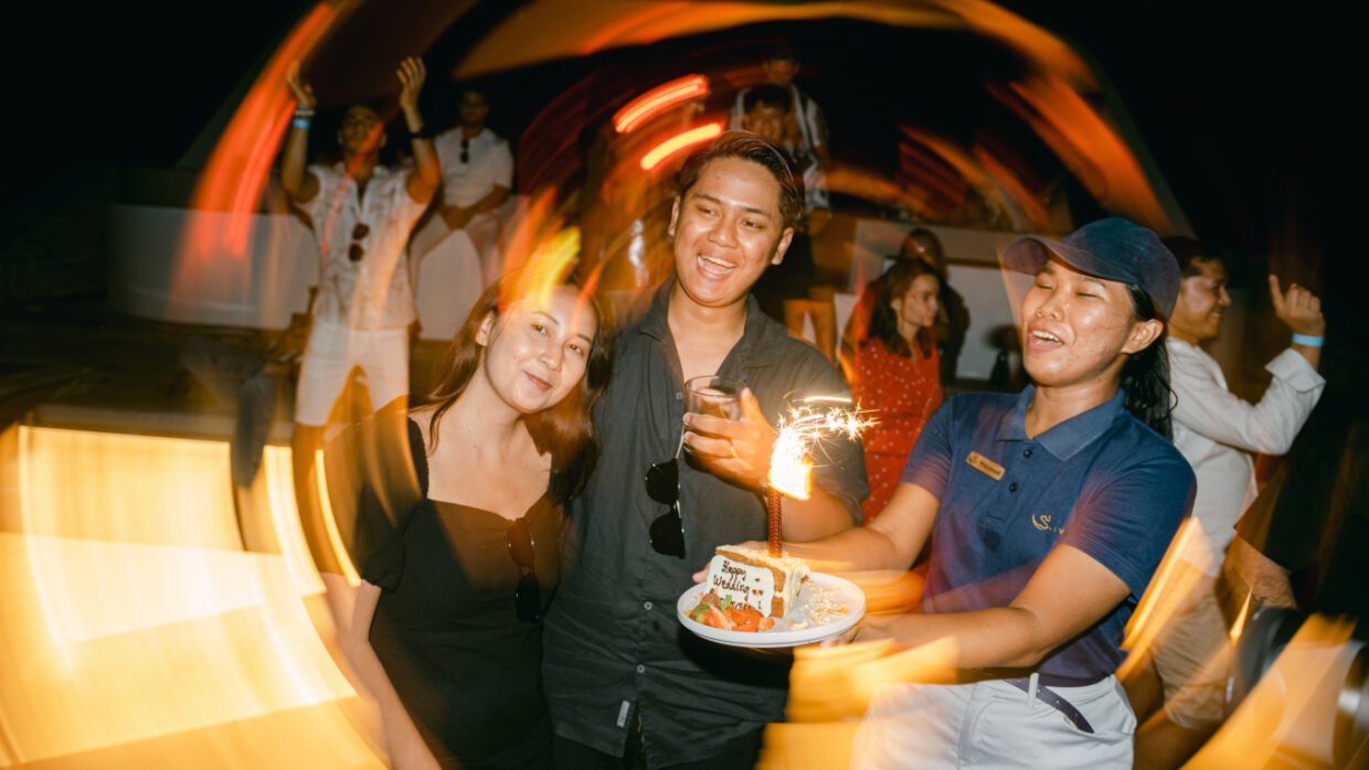 Crew presents a sparkler-topped anniversary cake to a smiling couple at a night party