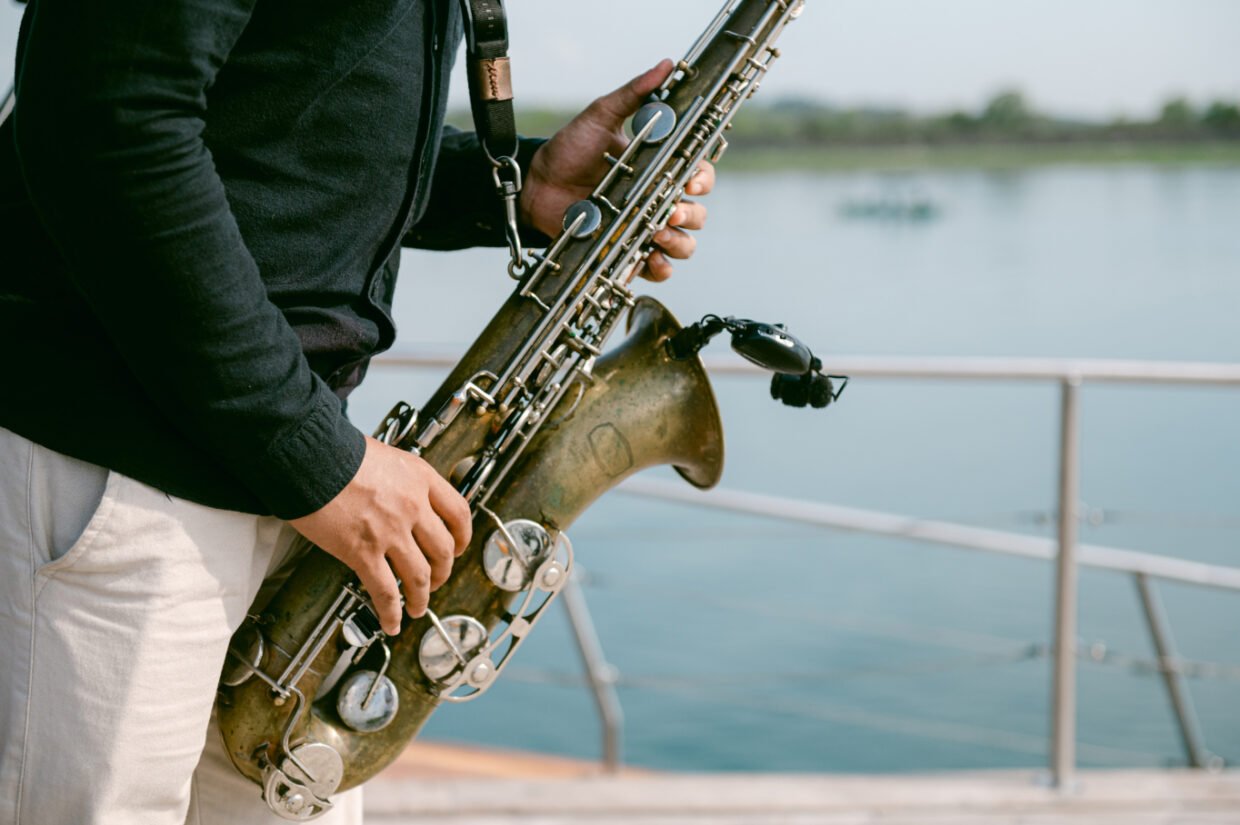 Saxophonist in black performing by the deck railing with calm water behind