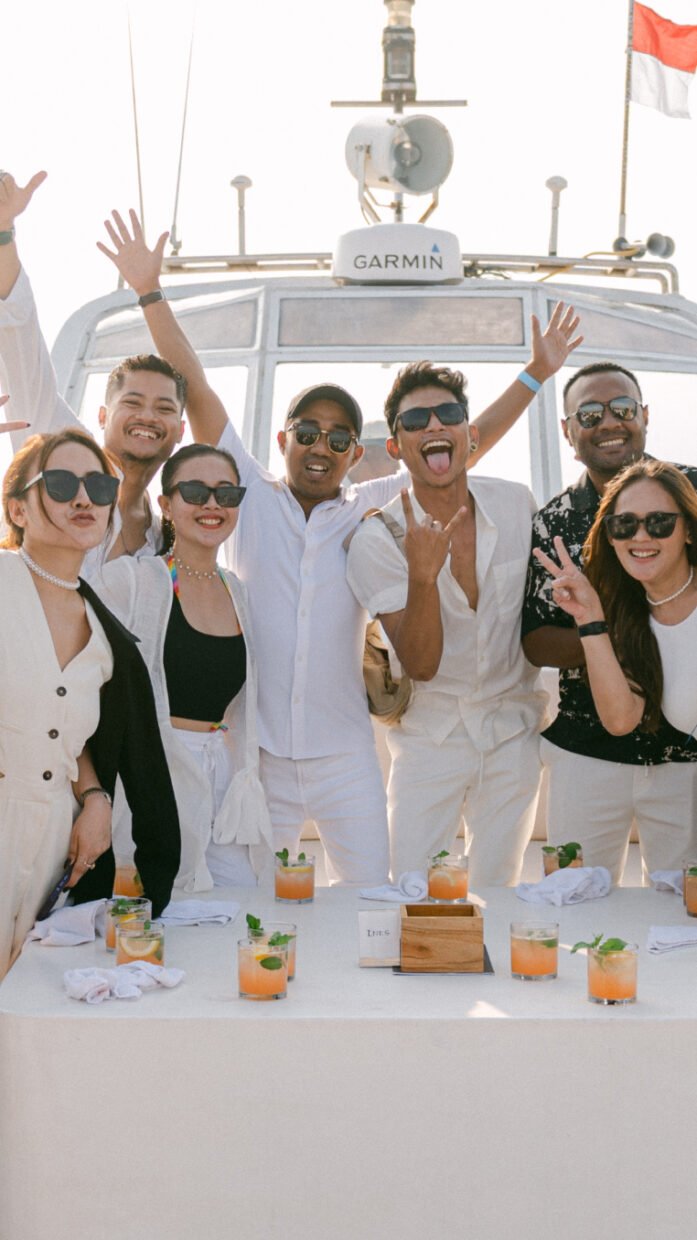 Friends in white cheering behind a cocktail-set table on the flybridge at golden hour