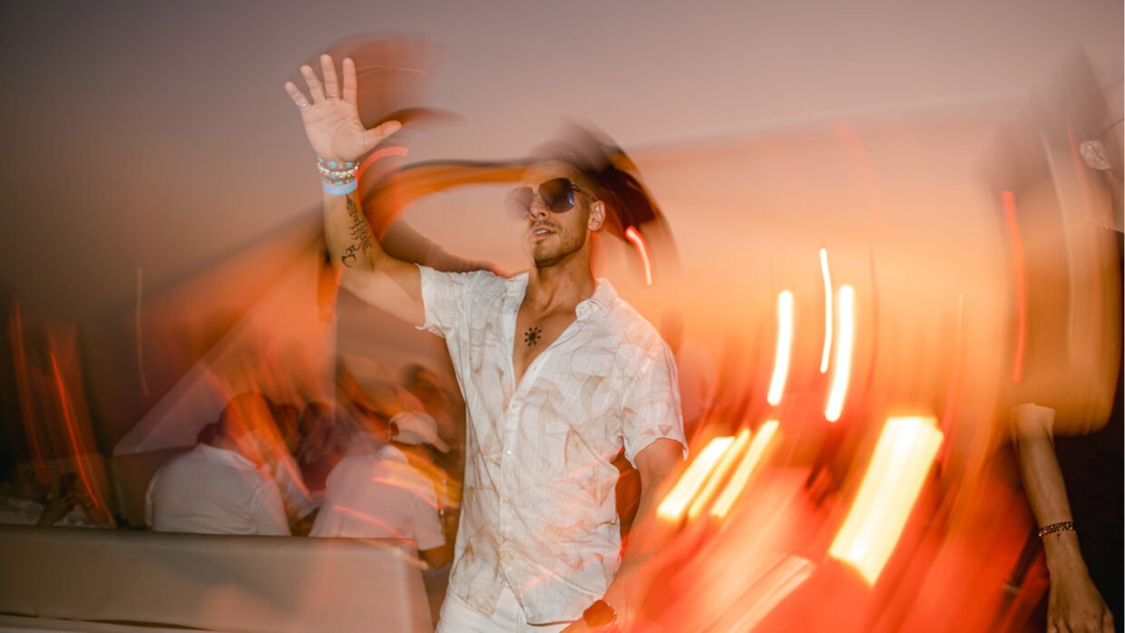 Man in white shirt and sunglasses dancing amid streaking party lights on deck
