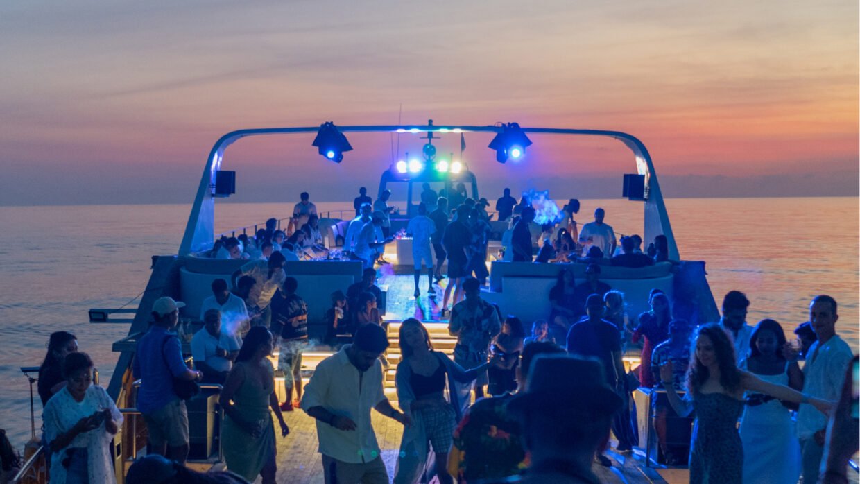 Crowd dancing on the open deck under stage lights at sunset