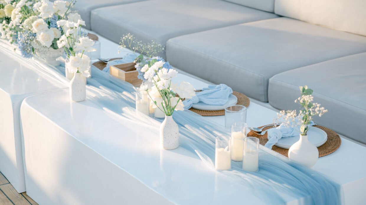Elegant blue-and-white floral table setting with candles along a deck lounge at sunset