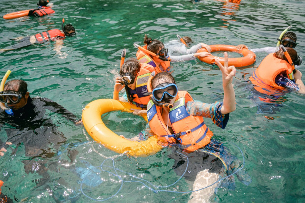 Snorkelers in orange life jackets floating with pool rings in clear green water