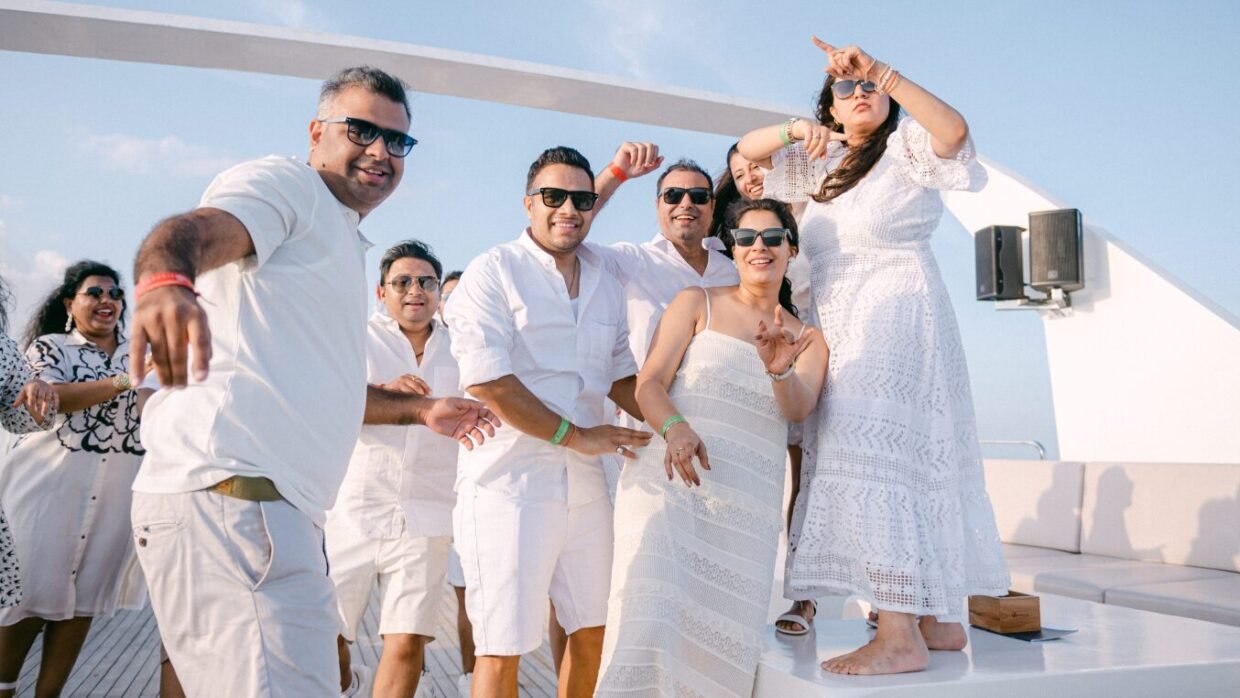 Group in white dancing and posing on the sunlit upper deck under a blue sky