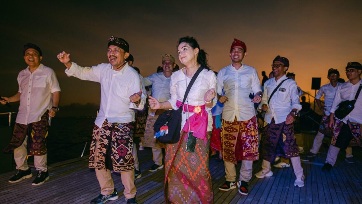 Guests in white and traditional Balinese sarongs dancing on deck at sunset