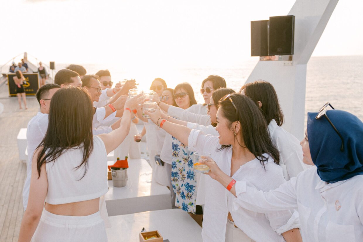 Guests in white raising a toast together on the deck in bright sunset light