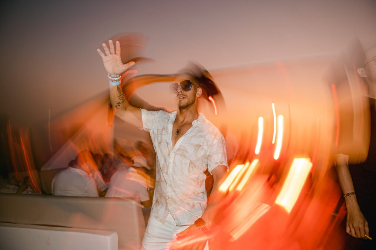 Man in white dancing among trailing light streaks at a sunset deck party