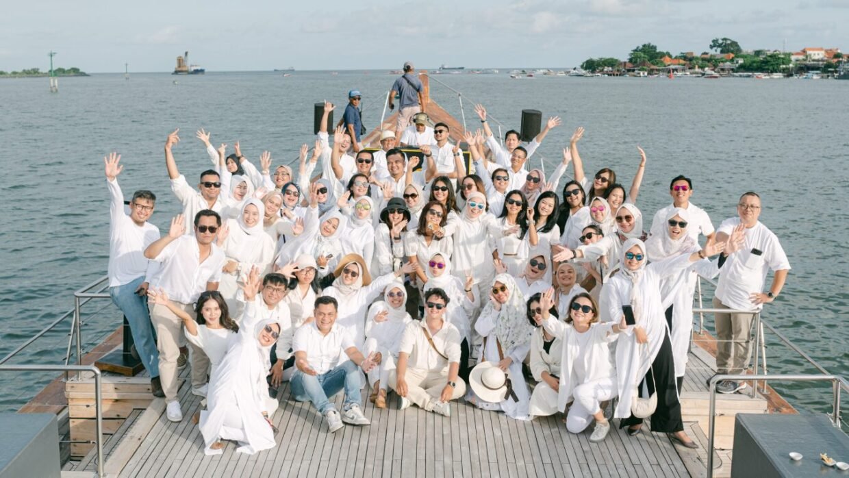 Large group in white waving from the yacht deck with Benoa harbour behind
