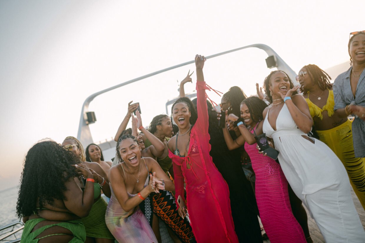 Women in colourful dresses laughing and dancing on deck at sunset
