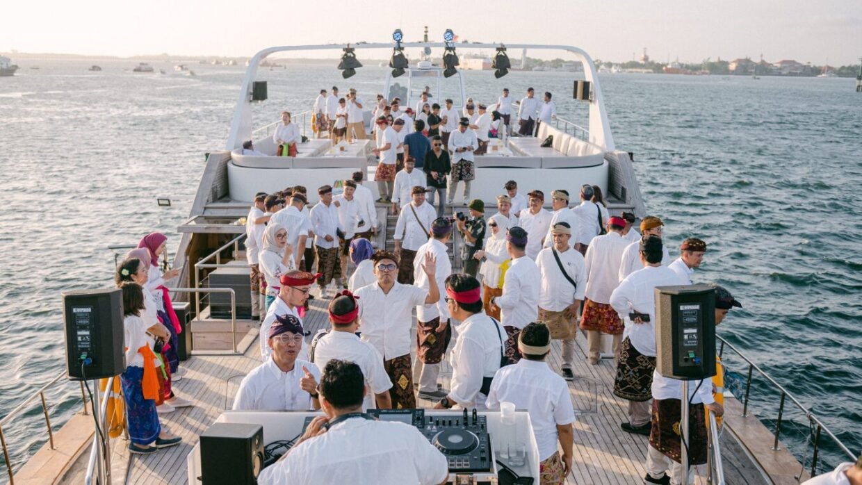 Guests in white and traditional sarongs gathered around a DJ on deck at golden hour