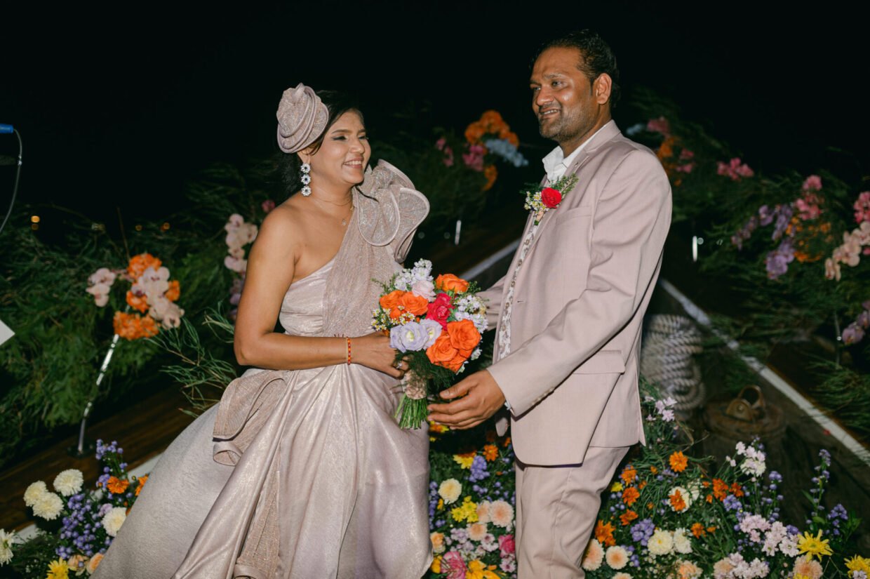 Smiling couple with bouquet at a floral-decorated onboard wedding ceremony at night