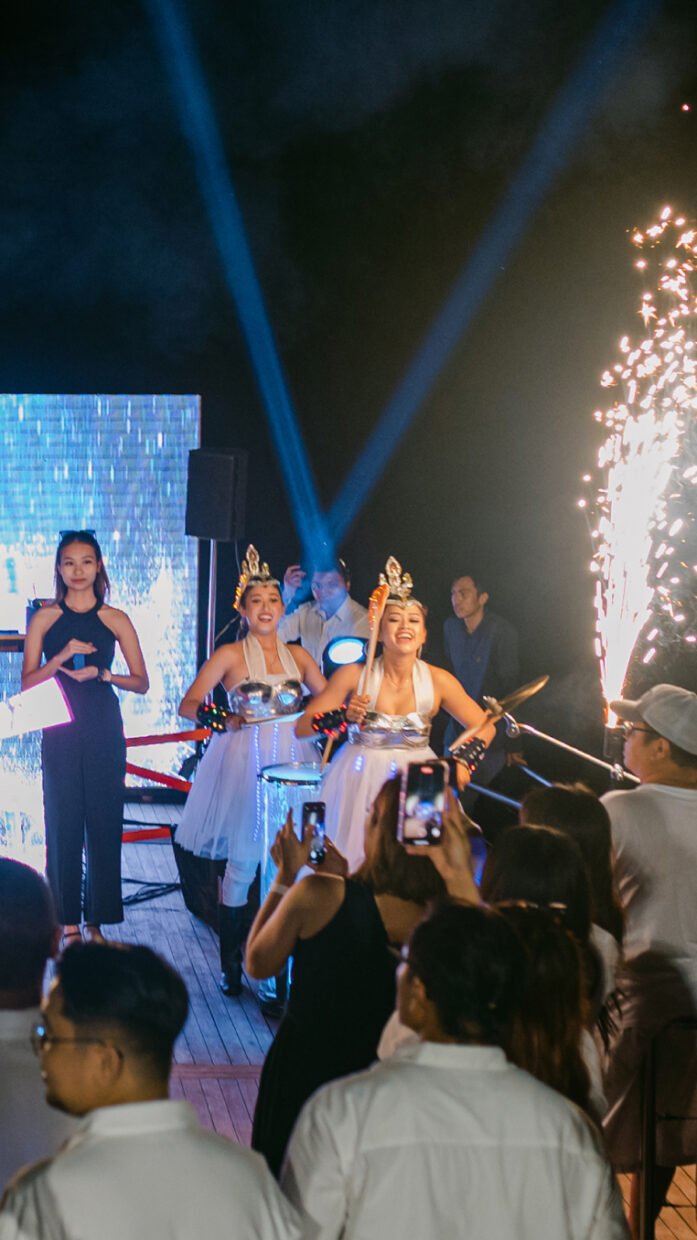Costumed performers with sparklers entering as guests film at an evening deck party