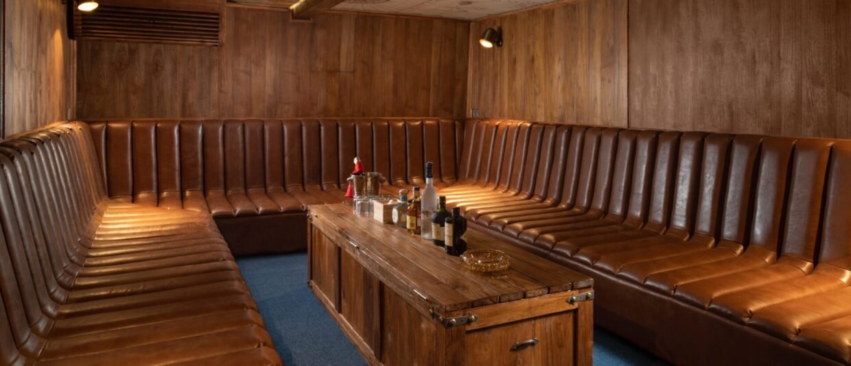 Wood-panelled lounge with tan leather bench seating and a central drinks table