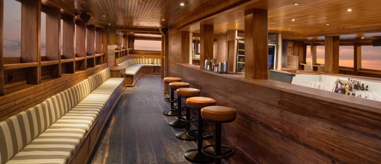 Timber interior bar with cushioned bar stools and striped banquette at sunset