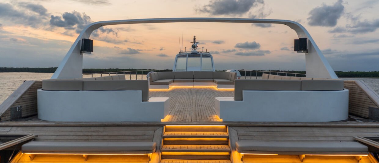 Upper deck sofa lounge with warm under-seat lighting and the helm station at sunset