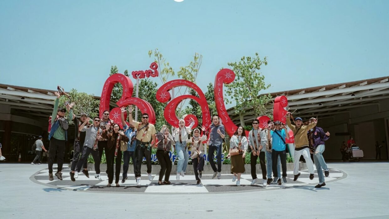 Group of people jumping in front of a large red Bali sign outdoors
