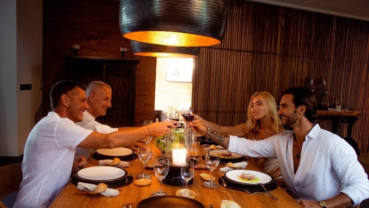 Four people enjoying a cozy indoor dinner, toasting with wine at a wooden table
